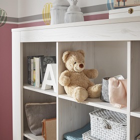 Offenes Regal in einem Kinderzimmer mit einem Teddy, Büchern und Accessoires.