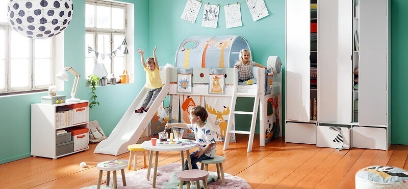 Spielende Kinder auf einem Spielbett mit Rutsche, Bogenzelt über der Liegefläche und Kindertisch mit Hockern.