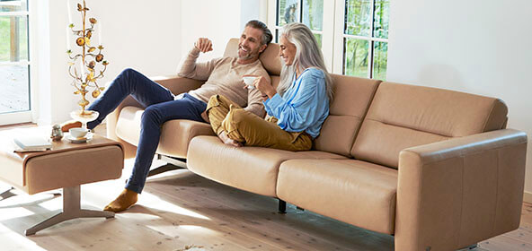 Ein Paar sitzt im Wohnzimmer auf einer hellen Ledercouch