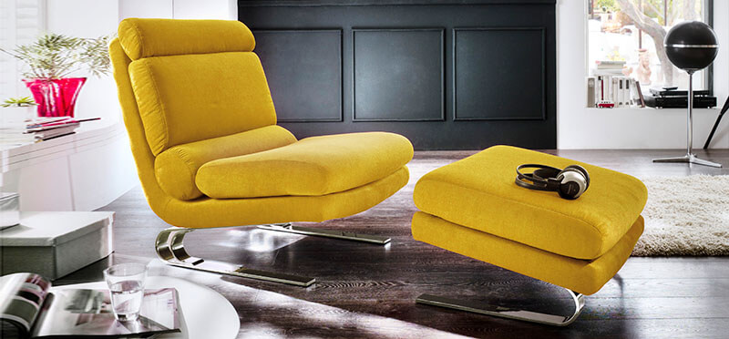 Gelber Sessel mit Beinablage auf dunklem Holzboden