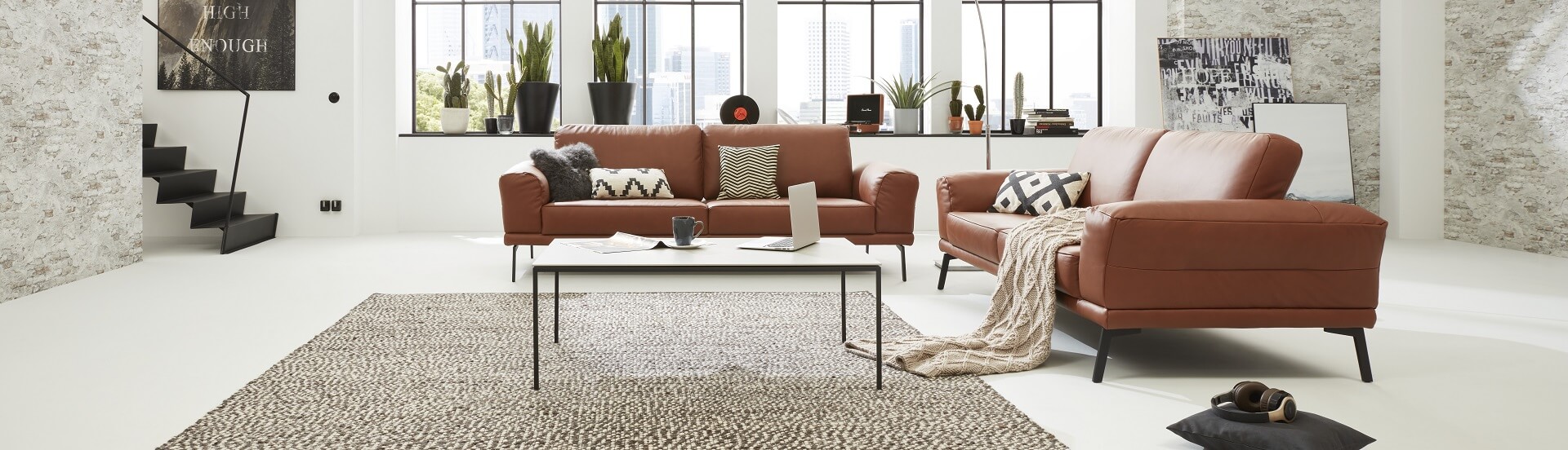 Ein großzügiges Wohnzimmer mit zwei Interliving Sofa Serie 4102, die über Eck stehen. Passende Kissen und eine Kuscheldecke strömen elegante Gemütlichkeit aus.