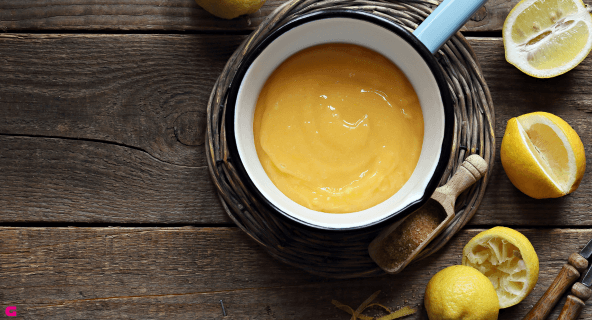 Ein Topf mit Lemon Curd und ausgepressten Zitronen daneben