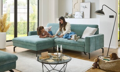 Mutter und ihre kleine Tochter sitzen auf einem türkisgrünen Sofa und blicken sich an.