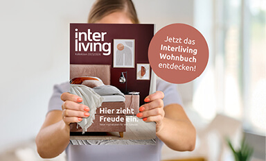 Frau hält einen Katalog mit Möbeln vor ihrem Gesicht in die Kamera.