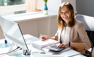 Das Bild zeigt eine junge Frau am Schreibtisch mit Taschenrechner und Unterlagen