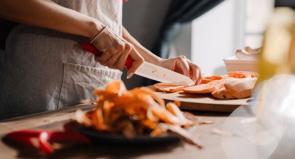 Hände schneiden Süßkartoffelscheiben für selbstgemachte Gemüsechips aus dem Backofen mit ingetriertem Airfryer.