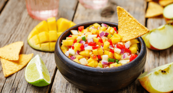 Bunte Mango-Salsa mit roter Paprika und Zwiebeln in einer Schüssel, Tortilla-Chips daneben