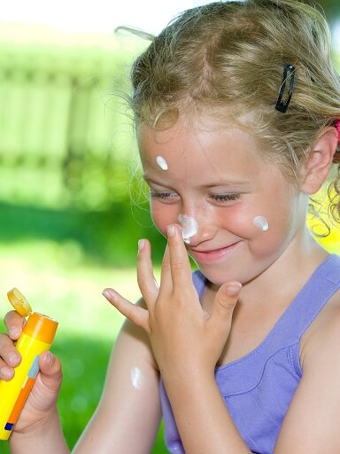 Sonnenschutz: ein Mödchen cremt sich mit Sonnencreme ein.