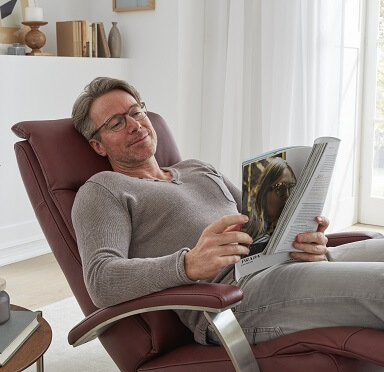 Ein Mann liegt entspannt in einem weinroten Comfortmaster -Relaxsessel und liest eine Zeitschrift.