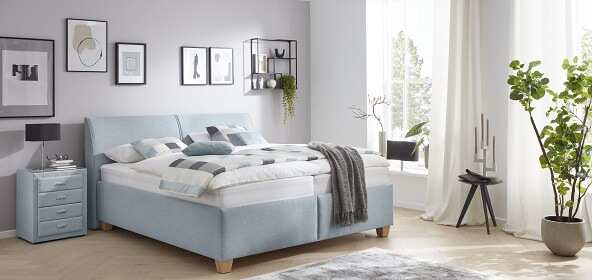 Möbel GUNST - Comfortmaster: Ein hellblau bezogenes Polsterbett mit Nachtisch im gleichen Design.