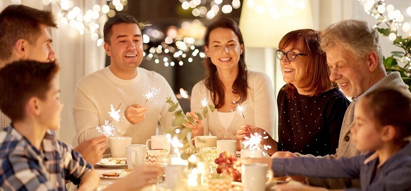 Eine Familie sitzt am festlich gedeckten Tisch und lässt Wunderkerzen leuchten.