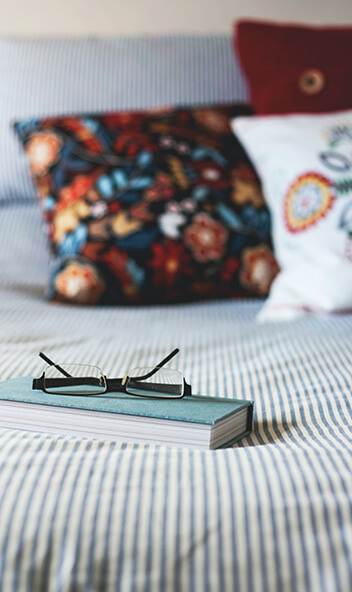 Buch und Brille liegen auf einem Bett.