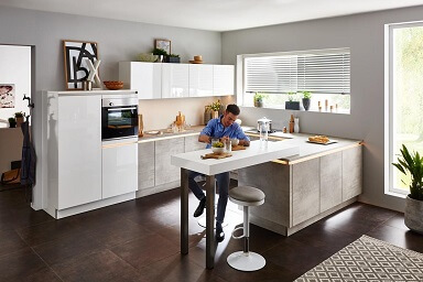 GUNST-Ratgeber Küchenstil: Ein Mann sitzt an einem verlängerten Tresen in einer Küche in Weiß und Betonoptik.
