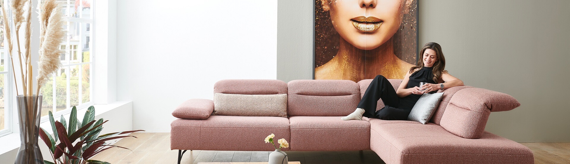 GUNST Blog "Zeit für Komfort" - eine Frau sitzt langestreckt auf einem roséfarbenen Sofa, hat einen Arm an die Rückenlehnen angelehnt und blickt in ihr Mobiltelefon.