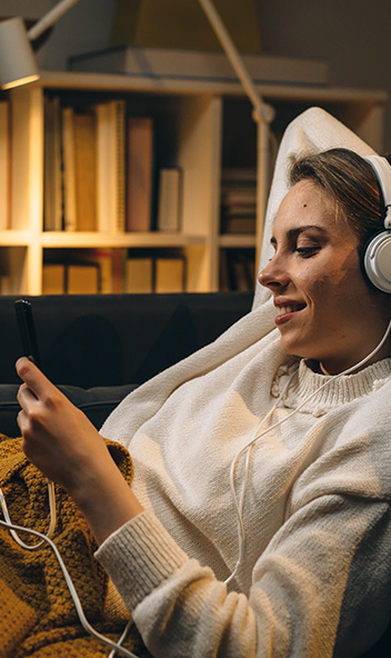 Eine Frau liegt entspannt in einem Relaxsessel und hört Musik mit Kopfhörern. 