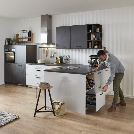 Moderne L-Küche, die sich zum Wohnbereich in einem überbreiten Inselelement öffnet. So entsteht zusätzlicher Stauraum unter der Arbeitsfläche.