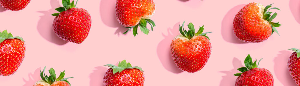 Erdbeeren mit Grün lose verteilt vor roséfarbenem Hintergrund.