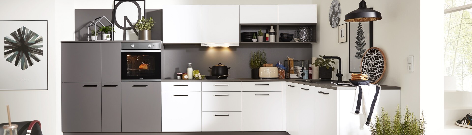 Einr ansprechende L-Küche in Weiß und Grau mit schwarzen Deko-Accessoires.