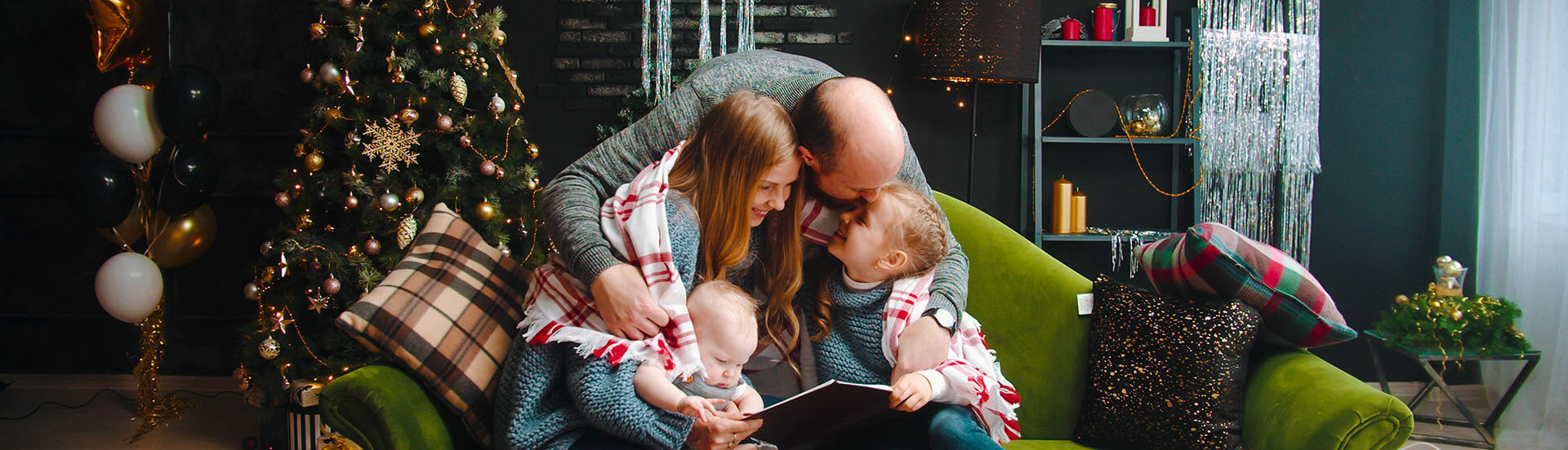 Weihnachtsliches Ambiente, ein Vater lehnt sich über ein Sofa und umarmt seine FAmilie.