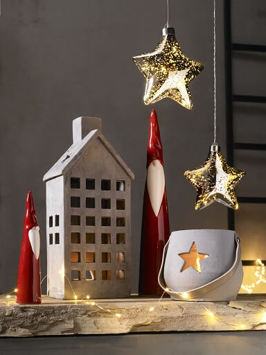 Deko-Arrangement mit Holzhäussche, zwei Weihnachtsmännern aus prozellan und einem Windlicht mit Stern.