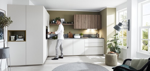 Bei dieser L-Küche wurden Oberschränke und ein Regal üfer dem Kochfeld in Holzoptik gehalten, während die restlichen Küchenmöbel in einem sehr hellen Grau gehalten sind. 