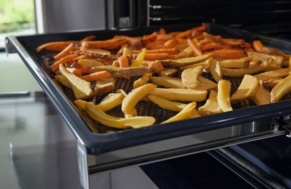 Süßkartoffelspalten und Kartoffelspalten auf einem Backblech für Gemüsechips aus dem Backofen mit integriertem Airfryer.