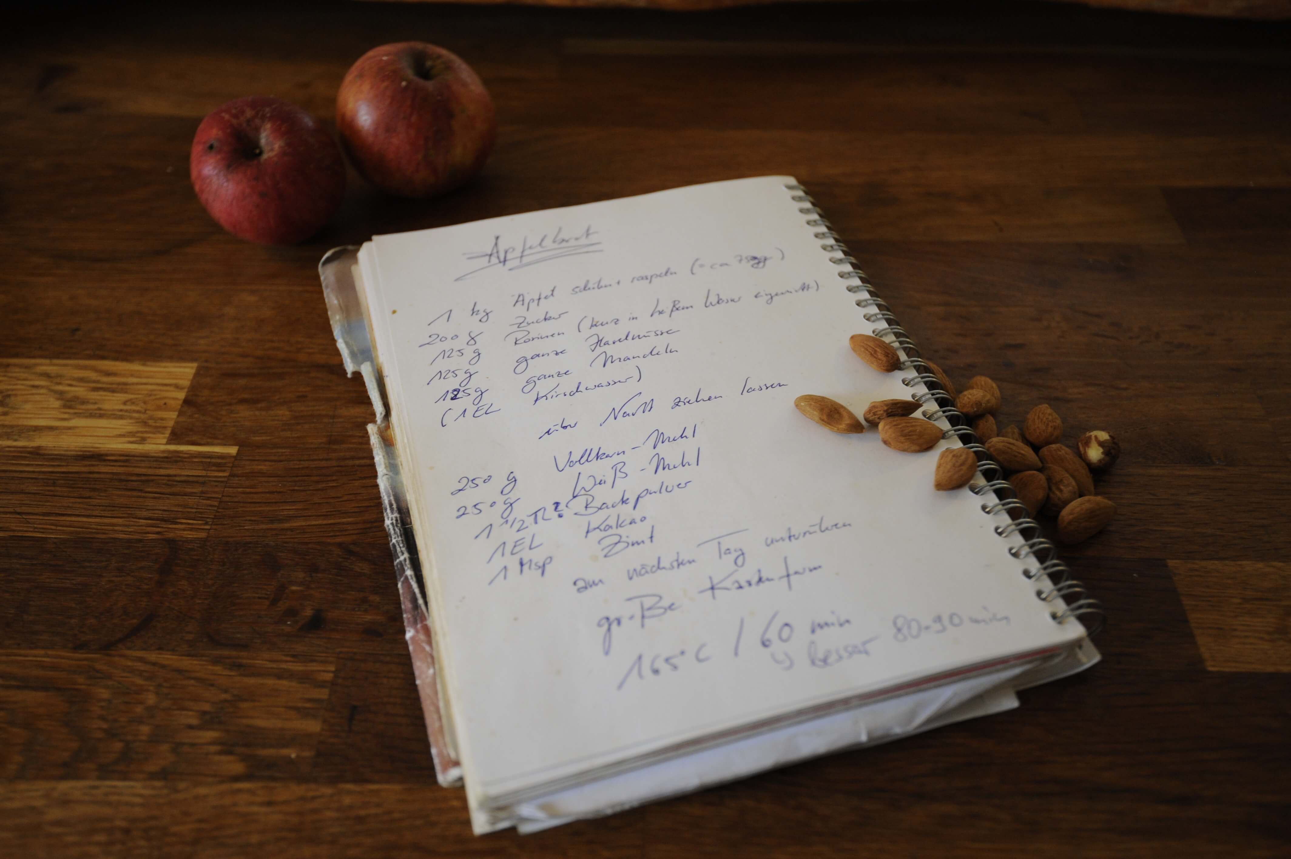 Ein handgeschriebenes Rezept in einem Ringbuch, darum Manelnd und Äpfel