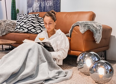 Herbstzeit ist Kuschelzeit: Eine Frau hat es sich mit einer Kuscheldecke, einem buch und einem Glas Wei ngemütlich gemacht.