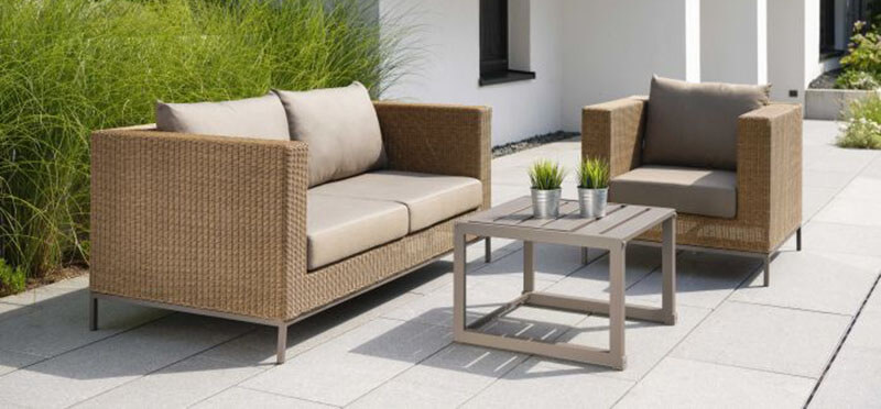 Garten-Lounge mit kubischen Gartenmöbeln aus helem Polyrattan und niedrigem Beistelltisch.